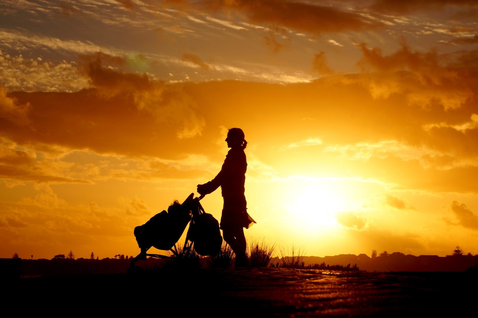 Mother with pushchair silhouetted against sunset