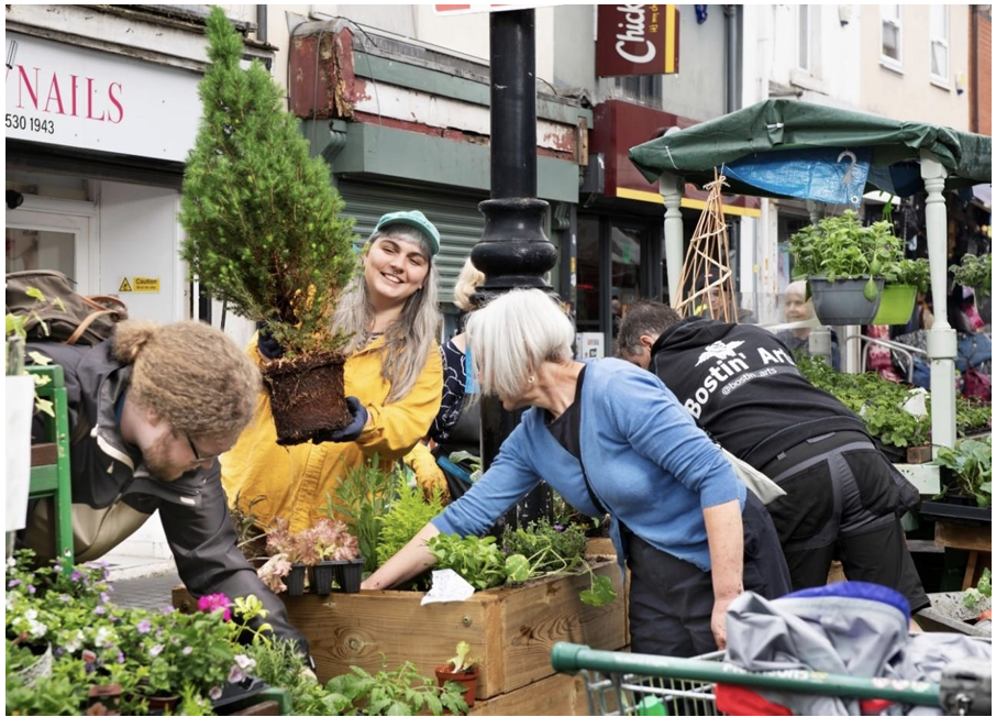 Image of smiling people planting a tree in a planter box on a street